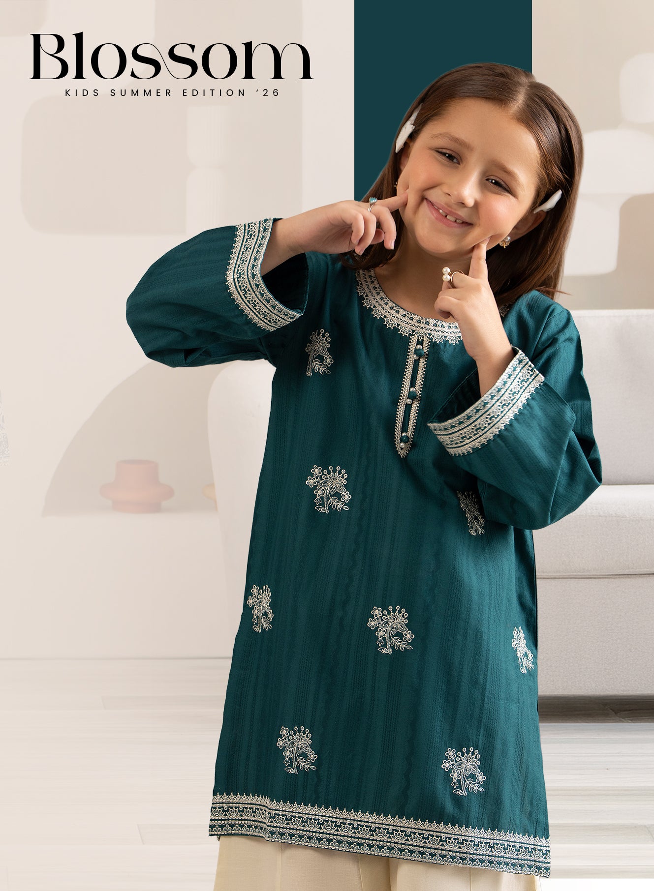 Young girl wearing a teal embroidered dress with a blurred indoor background